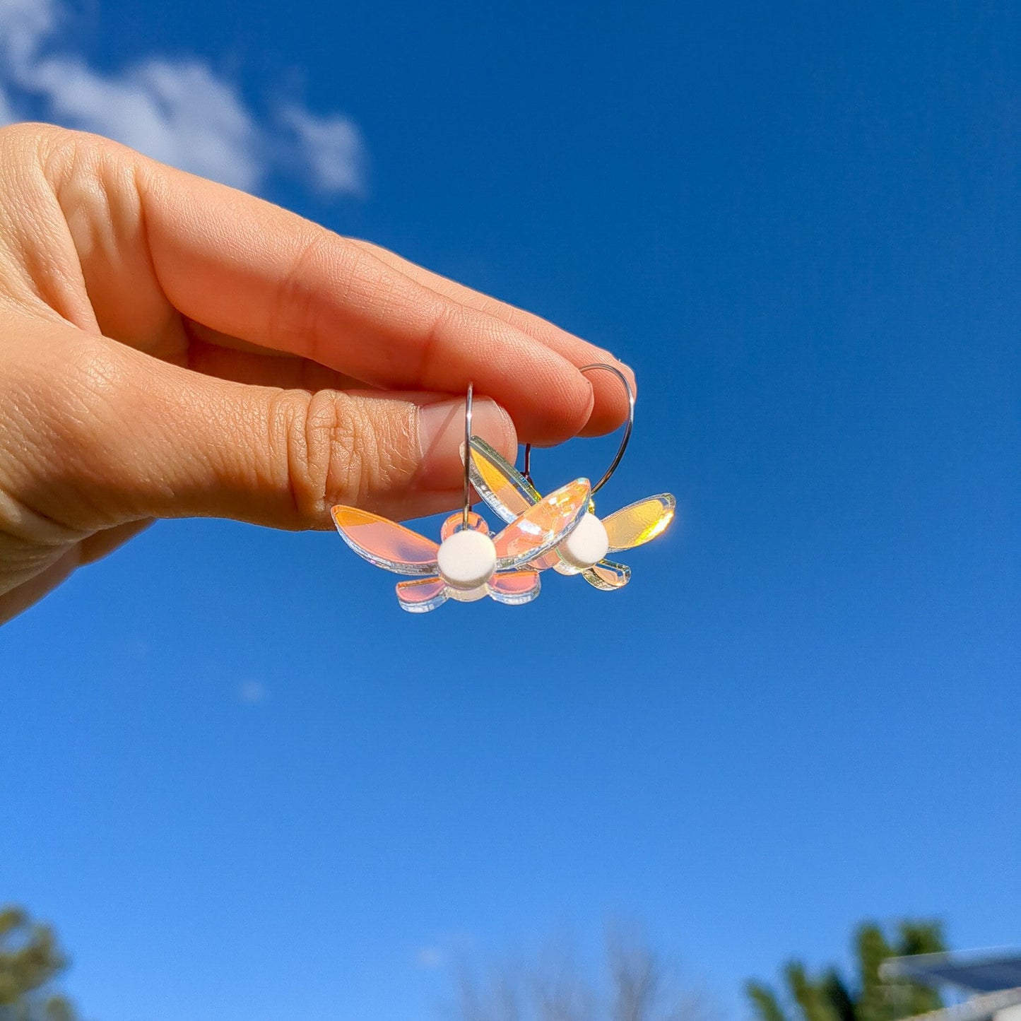Legend of Zelda Navi Fairy Acrylic on hoop earrings, held by a hand and hovering in the sky